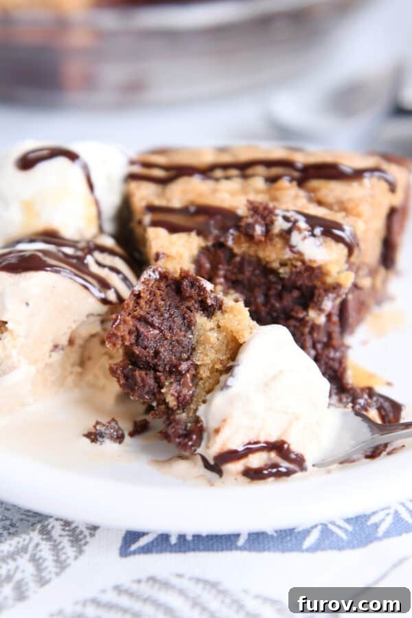 A delightful presentation of brookie pie, featuring a slice on a white plate drizzled with chocolate sauce, accompanied by a scoop of creamy ice cream.