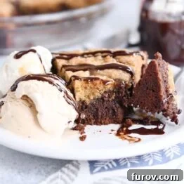 A bite of brookie pie is artfully cut out with a fork, placed on a white plate with ice cream and a delicate chocolate drizzle, creating an enticing visual.