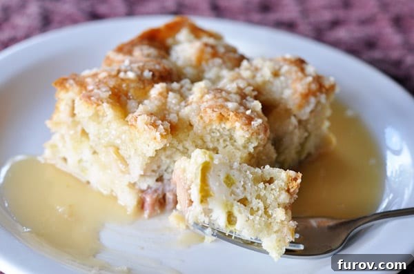 A delectable slice of Rhubarb Streusel Cake, rich with vibrant rhubarb and topped with a golden streusel, perfectly drizzled with warm vanilla sauce, with a fork poised for a bite.