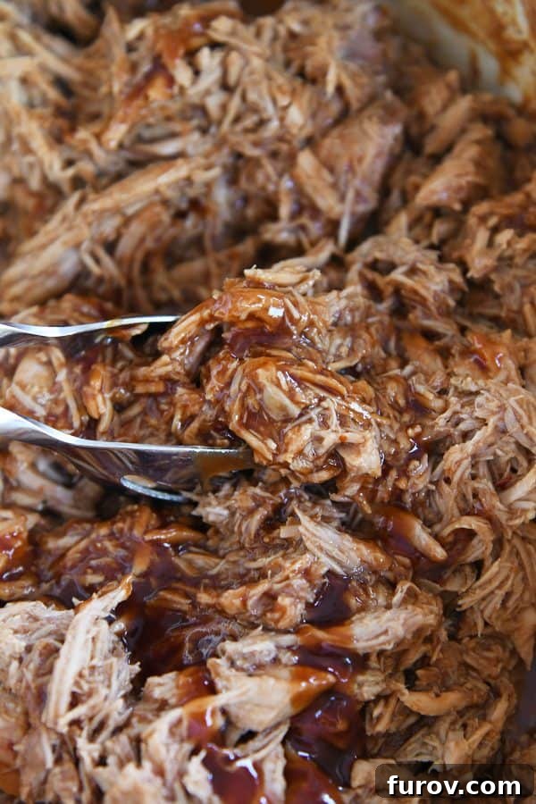 Close-up of cooked, shredded BBQ pork glistening with sauce, ready for serving.