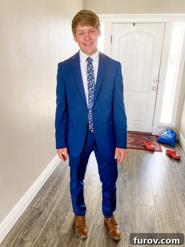 Teenager in a sharp blue suit stands confidently next to a wall, ready for prom
