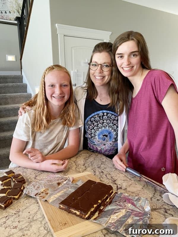 Three women standing in a kitchen, proudly displaying a pan of freshly made Nanaimo bars
