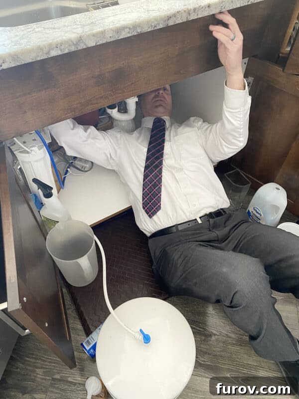 A man in a shirt and tie working diligently underneath a sink, fixing a garbage disposal