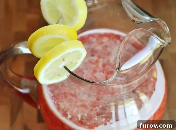 Luscious Strawberry Lemonade 2 Top view of a glass pitcher full of strawberry lemonade with lemon slices on the side of the pitcher.