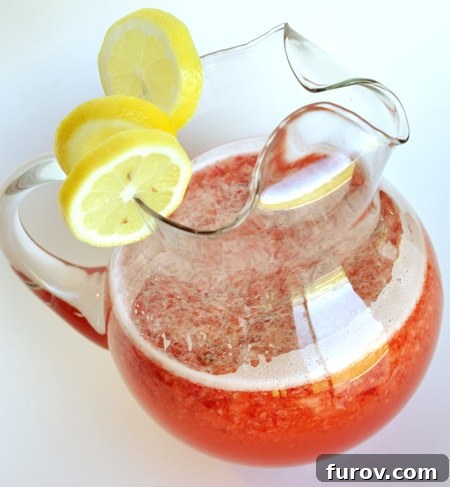 Luscious Strawberry Lemonade 3 Glass pitcher with lemon slices on top and half full of strawberry lemonade.