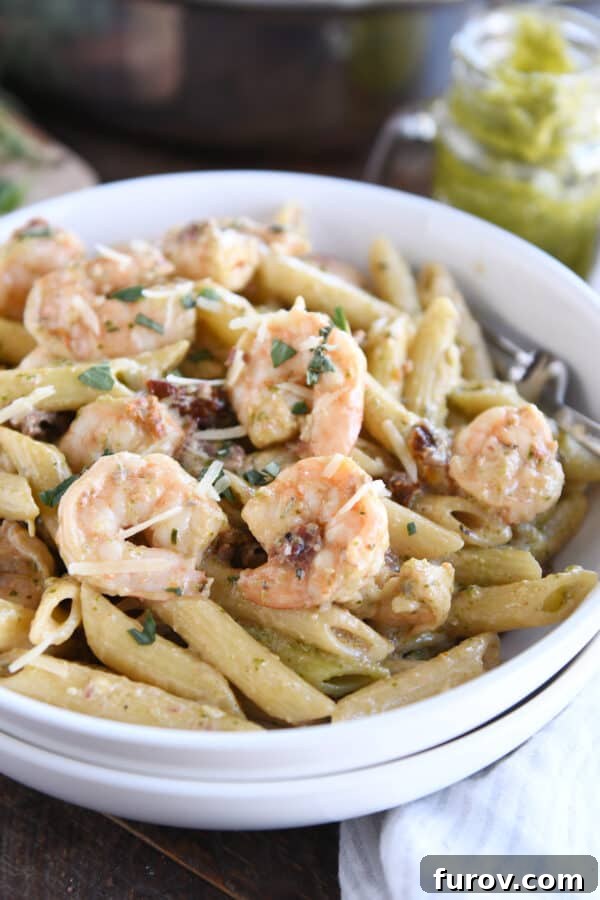Vibrant Pesto Shrimp Pasta with Sun Kissed Tomatoes 3 Shrimp, penne pasta, and sun-dried tomatoes served in two stacked white bowls.