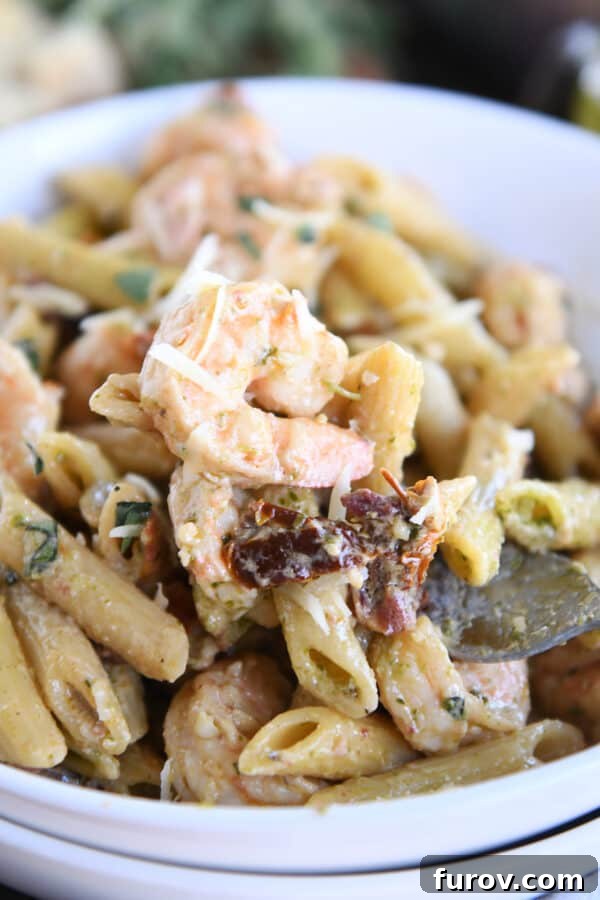 Vibrant Pesto Shrimp Pasta with Sun Kissed Tomatoes 5 A white bowl filled with shrimp, pasta, and sun-dried tomatoes, with a fork digging in.