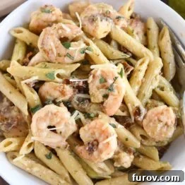 Vibrant Pesto Shrimp Pasta with Sun Kissed Tomatoes 7 pasta with shrimp, parmesan and sun-dried tomatoes in white bowl with fork