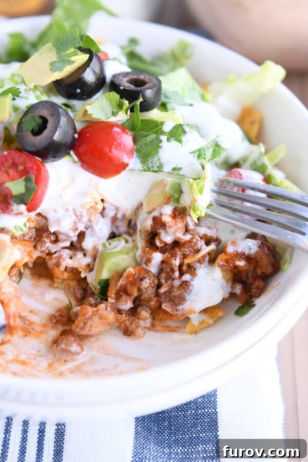 Elevated Taco Bowls with Zesty Creamy Lime Dressing Stovetop or Slow Cooker 3 Close-up of a white bowl overflowing with crunchy corn chips, a generous scoop of seasoned taco meat and rice, and a vibrant medley of fresh taco toppings, ready to be enjoyed.