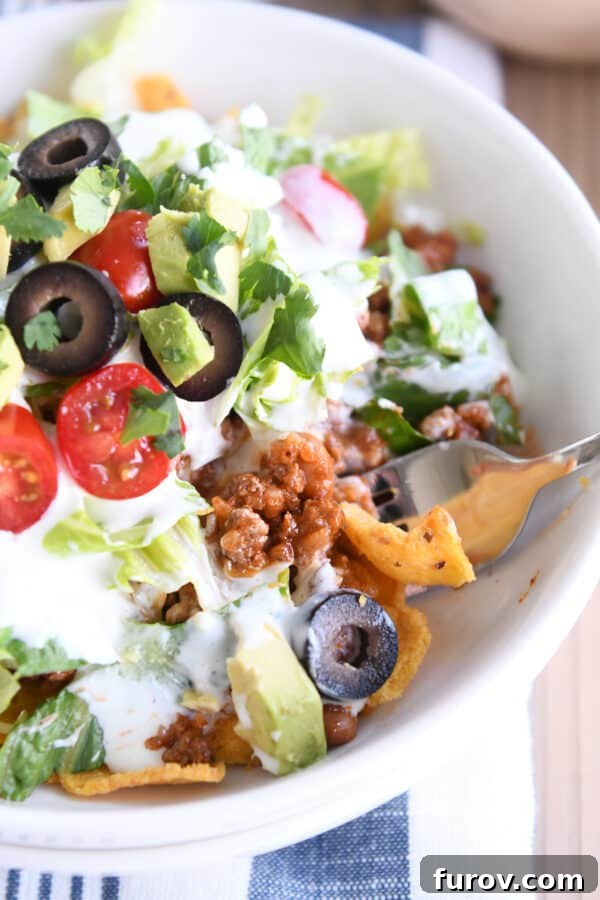 Elevated Taco Bowls with Zesty Creamy Lime Dressing Stovetop or Slow Cooker 8 A beautifully assembled Floating Taco Bowl featuring a base of crunchy corn chips, a hearty layer of taco meat, topped with fresh lettuce, shredded cheese, and vibrant toppings like diced tomatoes and olives, ready to be enjoyed.