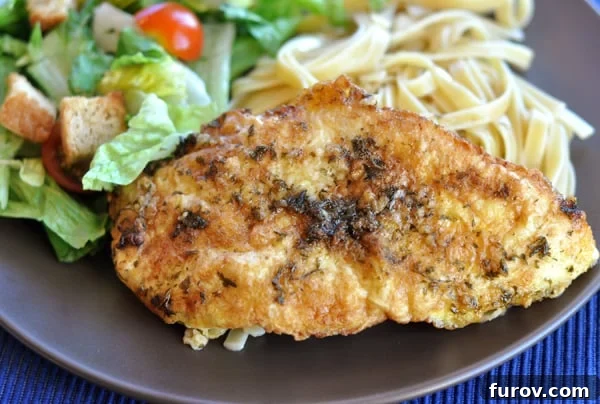 A dish of perfectly breaded chicken, accompanied by a fresh green salad and tender pasta, all drizzled with a rich lemon-butter sauce on a brown plate.