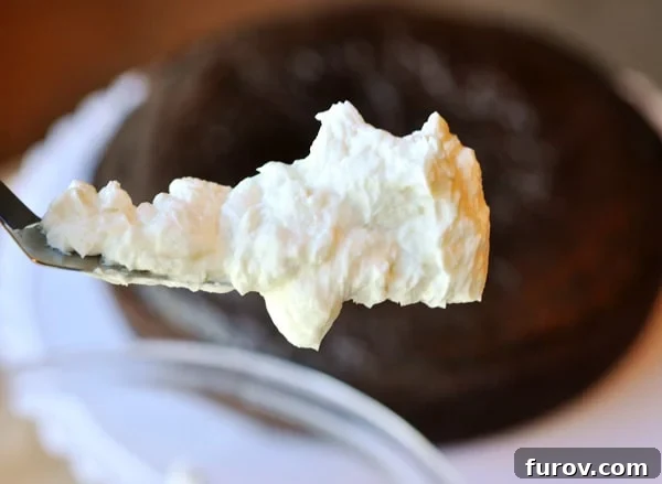 A scoop of white frosting on an offset spatula, with an unfrosted chocolate cake in the background. 