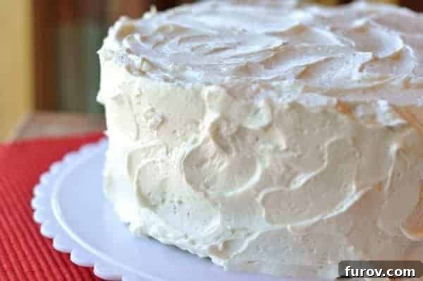 A two-layered cake cake sitting on a white cake platter, covered in white frosting. 