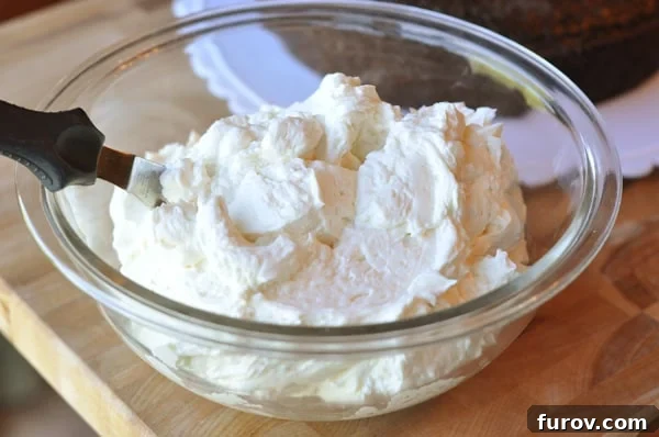 A glass bowl full of white frosting with an offset spatula inside the bowl. 