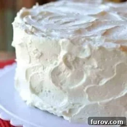 A two-layered cake cake sitting on a white cake platter, covered in white frosting. 