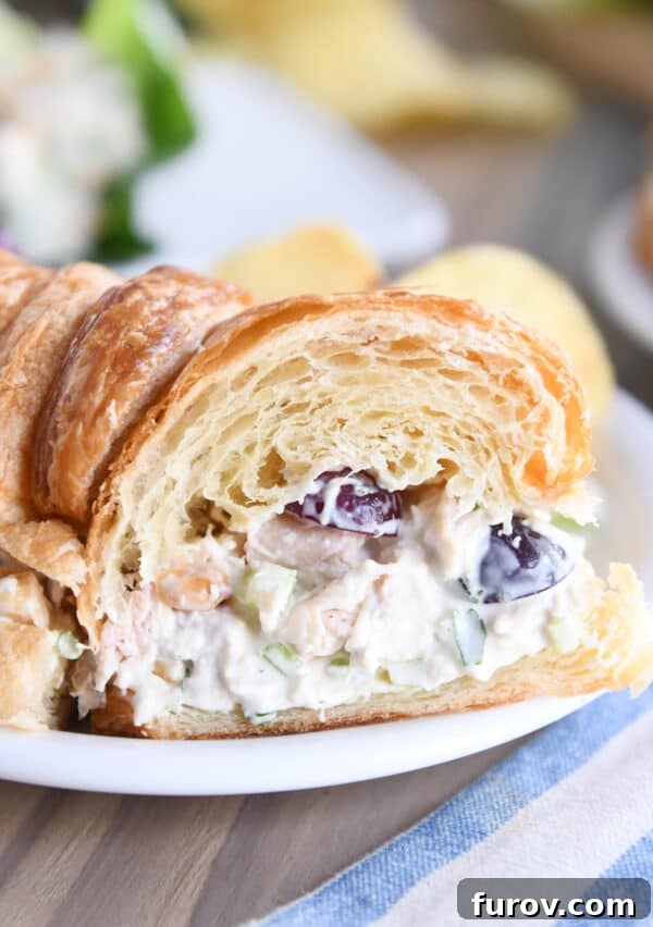 A perfectly prepared chicken salad sandwich on a flaky croissant, cut in half to showcase the rich, creamy filling and fresh ingredients.