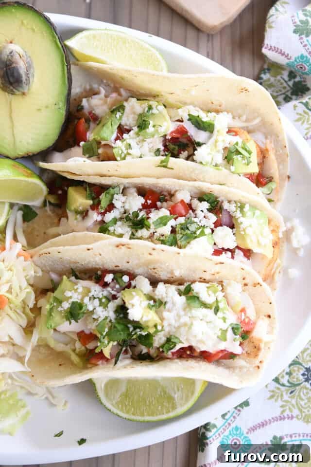 Three fish tacos on white platter with avocado and lime wedges.