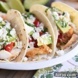 three fish tacos in corn tortillas on white platter