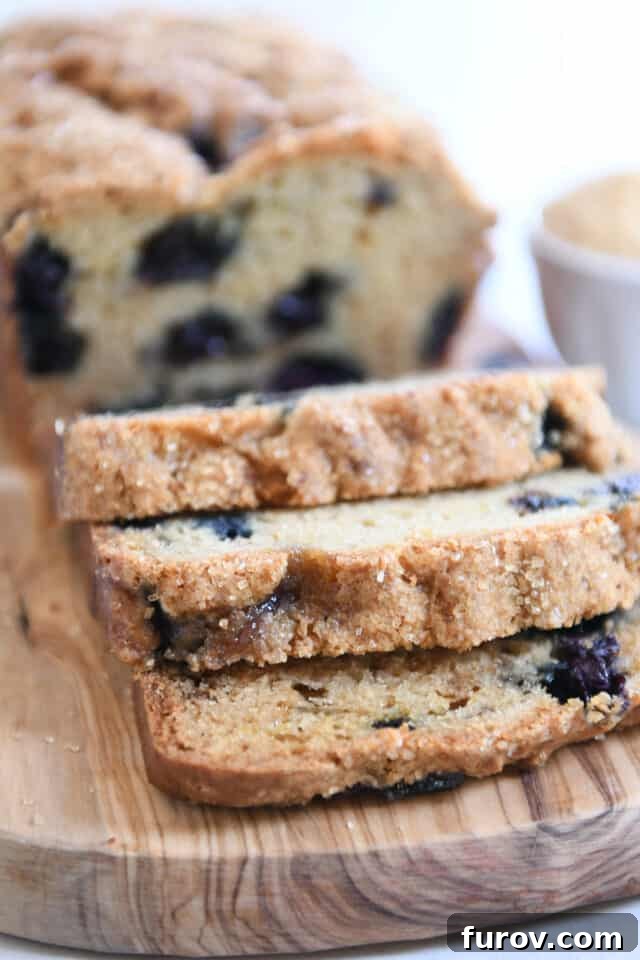 Three slices of blueberry muffin bread cut from the loaf on wood cutting board, showcasing the moist interior and blueberries.