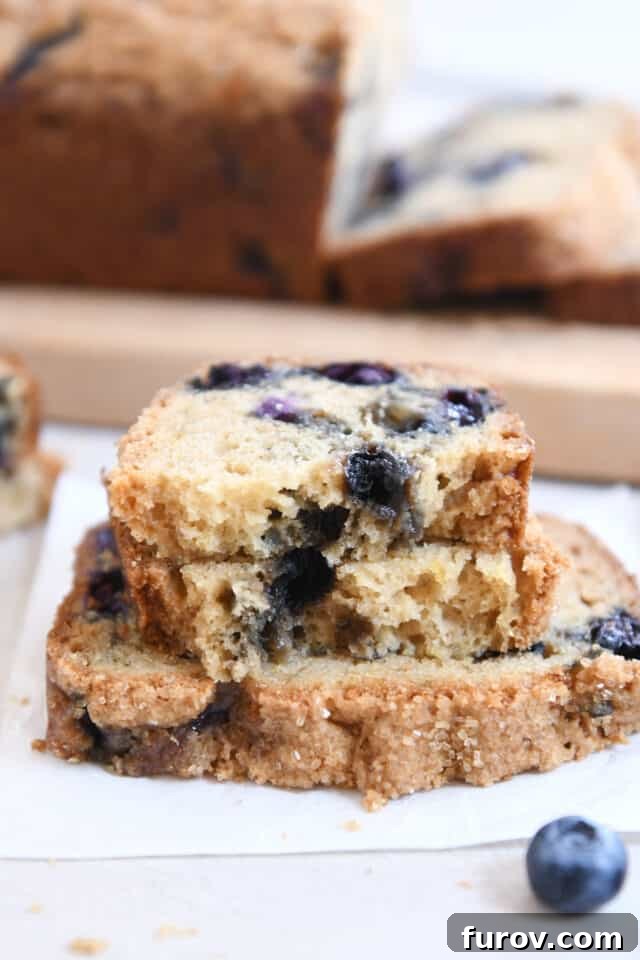 Two half slices of blueberry muffin bread artfully arranged on top of a full slice, highlighting the tender interior.