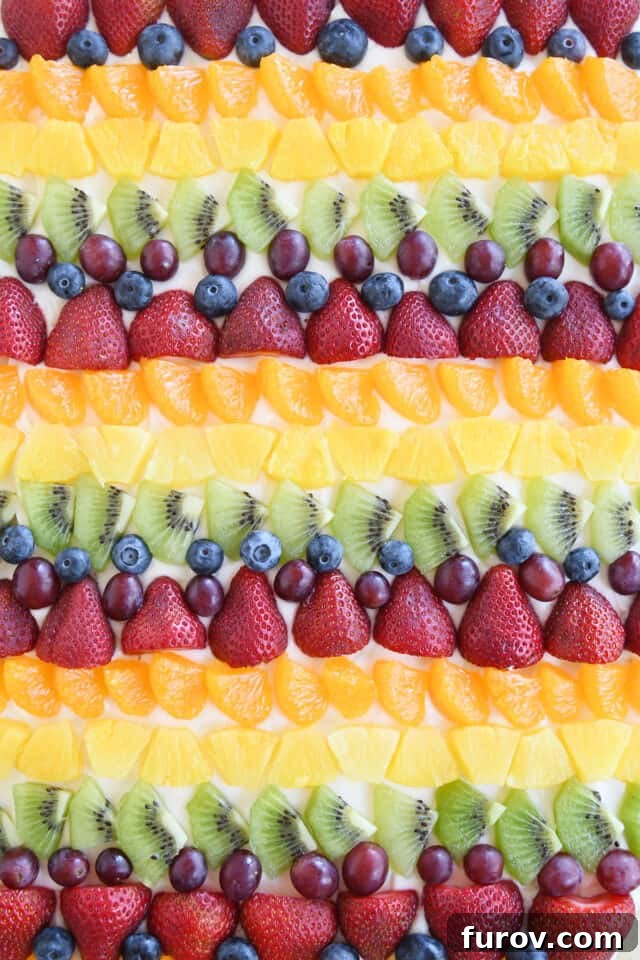 Rows of kiwi, red grapes, blueberries, strawberries, mandarin oranges and pineapple on fruit pizza.