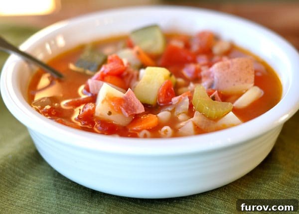 A beautiful white bowl brimming with vibrant red minestrone soup, showcasing a medley of fresh vegetables and small pasta. Perfect for a cozy autumn evening.