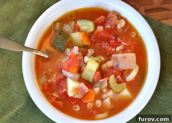 An overhead view of a rustic white bowl overflowing with a comforting autumn minestrone soup, rich with pasta and perfectly diced vegetables.