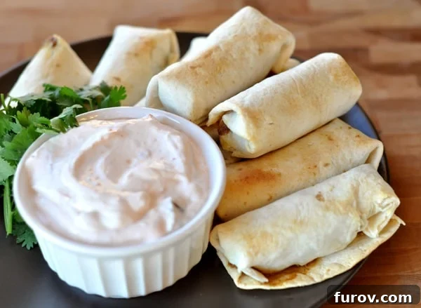 Golden brown cooked egg rolls surrounding a ramekin of creamy chipotle dipping sauce on a black plate.