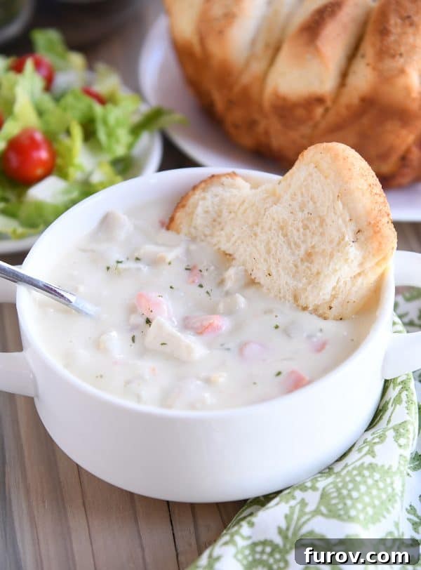 Cream cheese chicken vegetable soup with bread in white bowl.