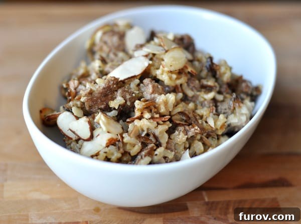 A close-up shot of the Wild Rice Hot Dish in an oval white bowl, highlighting the texture of the rice and the crunchy almond topping.