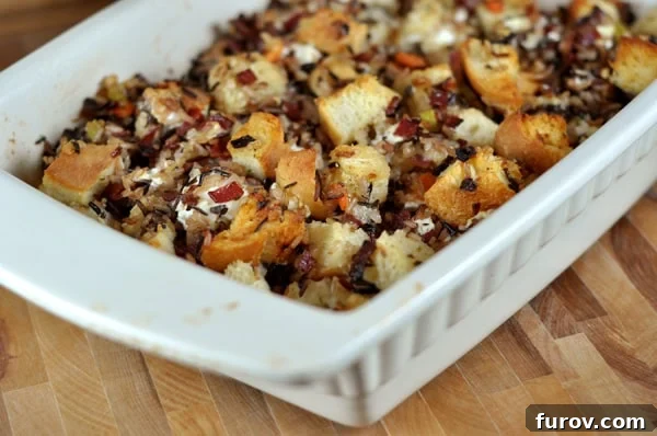 White casserole dish full of goat cheese and wild rice stuffing, garnished with fresh herbs.