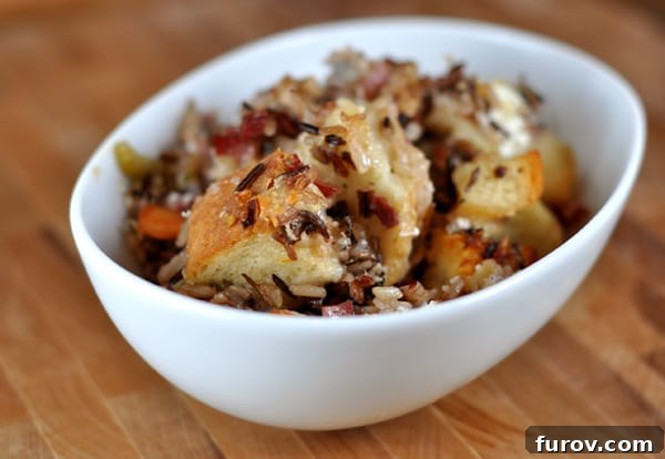 Close-up of wild rice stuffing in a white bowl, showing bread chunks and melted goat cheese.