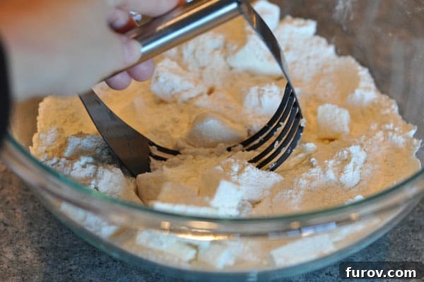 pastry blender blending cubed butter and flour in a glass bowl, creating coarse crumbs.