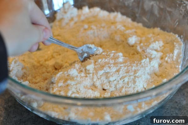fork mixing water and dough mixture together in a glass bowl, gentle tossing.
