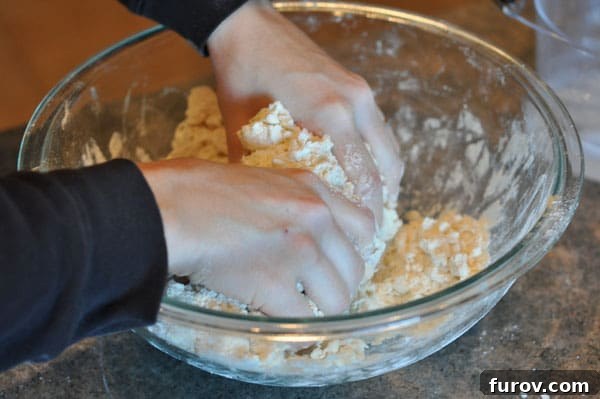 hands mixing dough in a glass bowl, ensuring butter stays cold.