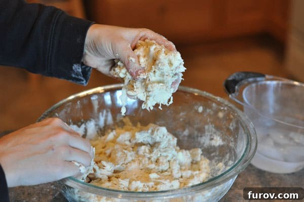 handful of dough over the top of a glass bowl of dough, showing crumbly texture.