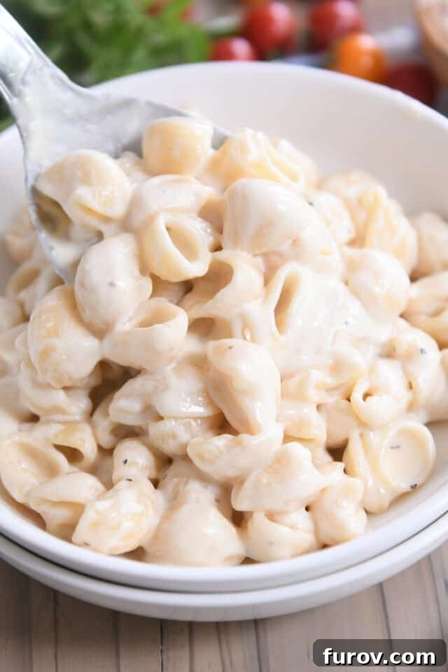 Spooning a generous helping of creamy Instant Pot Pasta Alfredo into a stack of white bowls, ready to serve.