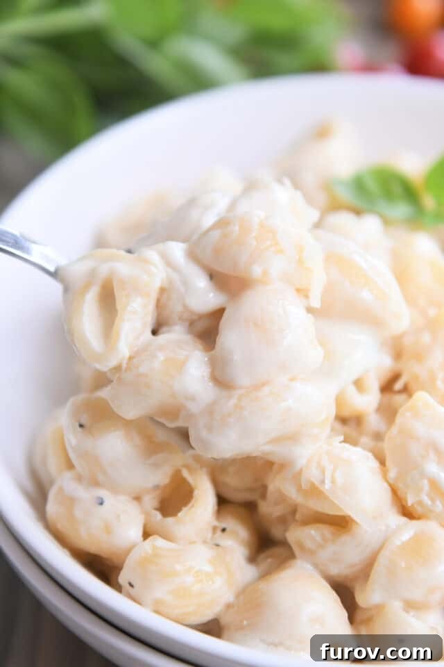 A spoon skillfully scooping up pasta shells generously coated in creamy alfredo sauce within a pristine white bowl.