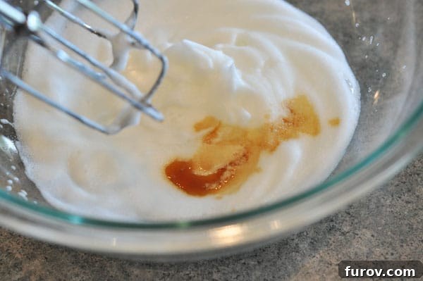 Vanilla extract being added to the stiffly beaten egg whites in a glass bowl.