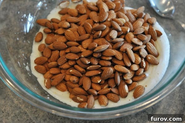 Raw almonds carefully placed on top of the stiff egg whites in a glass mixing bowl.