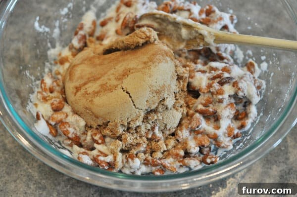 Egg white-coated almonds in a glass bowl, now topped with the brown sugar and cinnamon mixture.