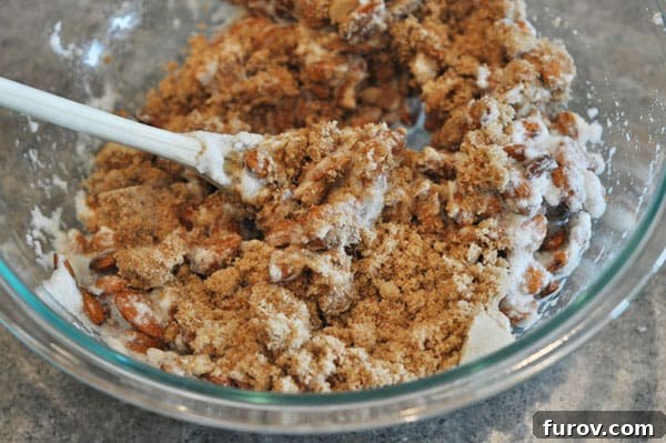 Almonds in a glass bowl, thoroughly coated with the brown sugar and cinnamon mixture, glistening and ready for baking.