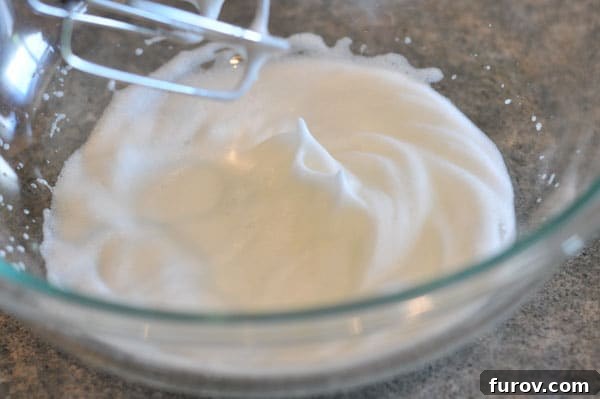 Perfectly whipped egg whites forming stiff peaks in a glass bowl, indicating they are ready for the next step.