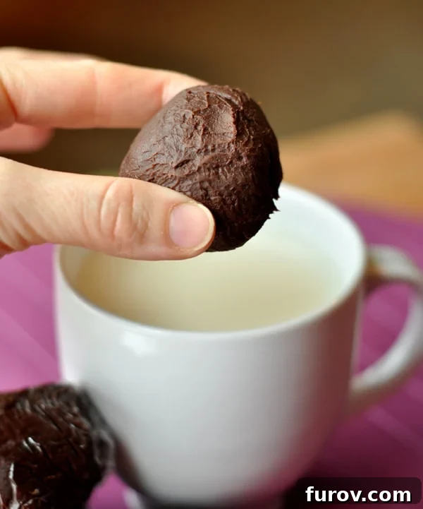 A hand holding a truffle hot chocolate ball over a white mug filled with milk, illustrating the preparation process.