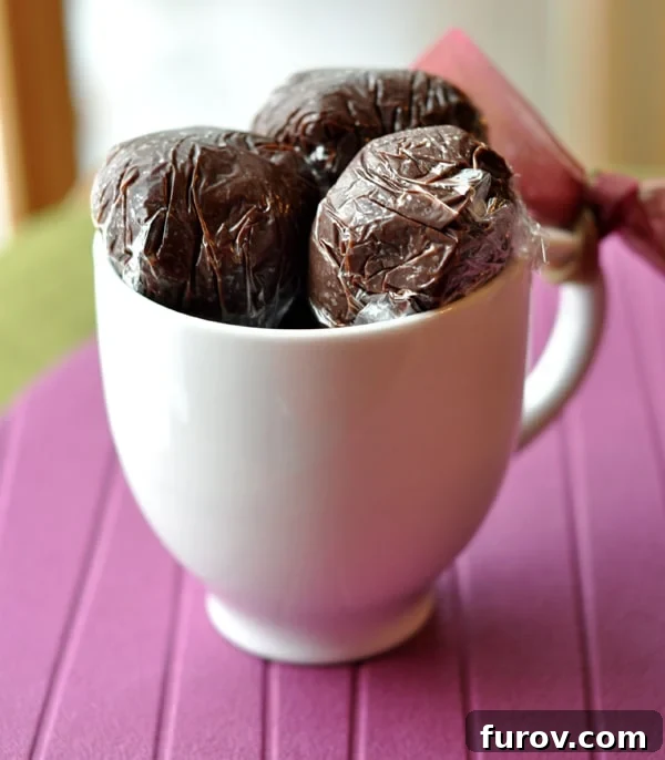 Saran wrapped hot chocolate truffle balls in a white mug, perfectly packaged for gifting.