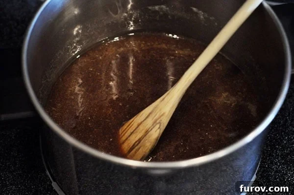 Melted sugar mixture in a saucepan with a wooden spoon, showcasing the smooth, dissolving consistency of the caramel.