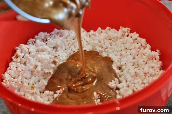 Rich caramel mixture being poured over a large red bowl of fluffy popped popcorn, ready for coating.