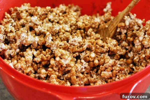 A vibrant red bowl now full of perfectly toffee-coated popcorn with peanuts, mixed and ready for baking.