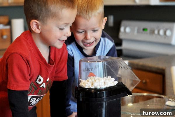 Two little boys happily watching popcorn popping in a popcorn maker, enjoying the process.