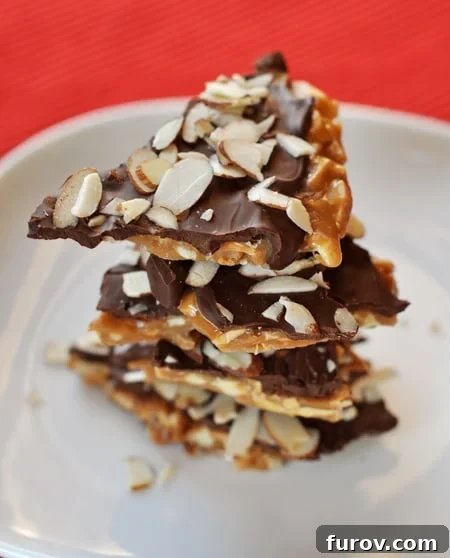 Delightful pieces of homemade almond roca, stacked invitingly on a pristine white plate, showcasing their rich chocolate and almond topping.